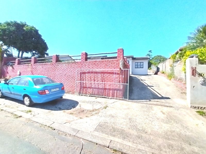 Front exterior view showing a concrete driveway, metal gate, and red brick boundary wall leading to the property entrance.