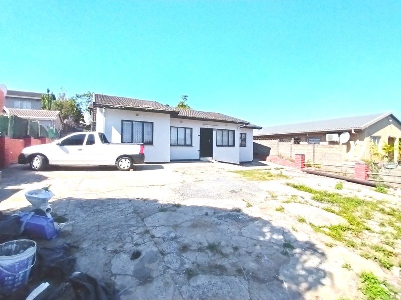 Front exterior view of a single-story house featuring a tiled roof, security bars on windows, and a large concrete driveway area.