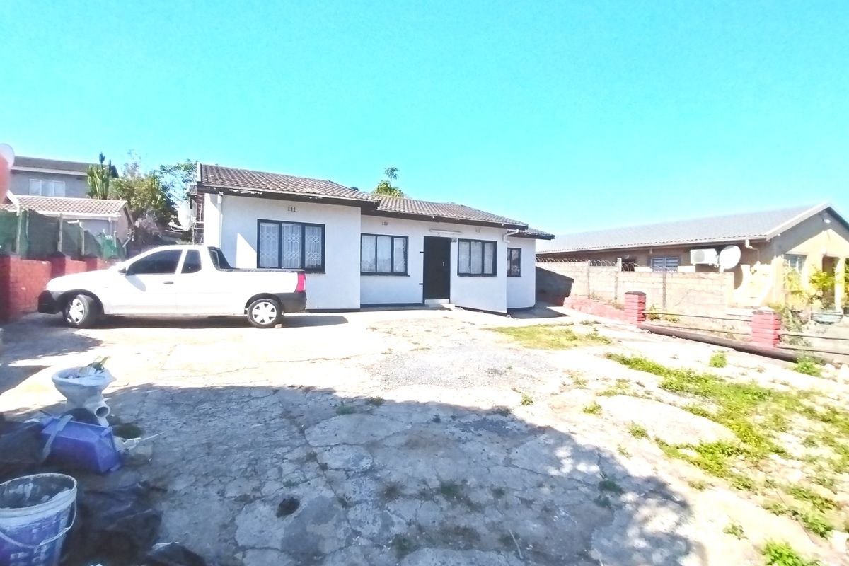 Front exterior view of a single-story house featuring a tiled roof, security bars on windows, and a large concrete driveway area.