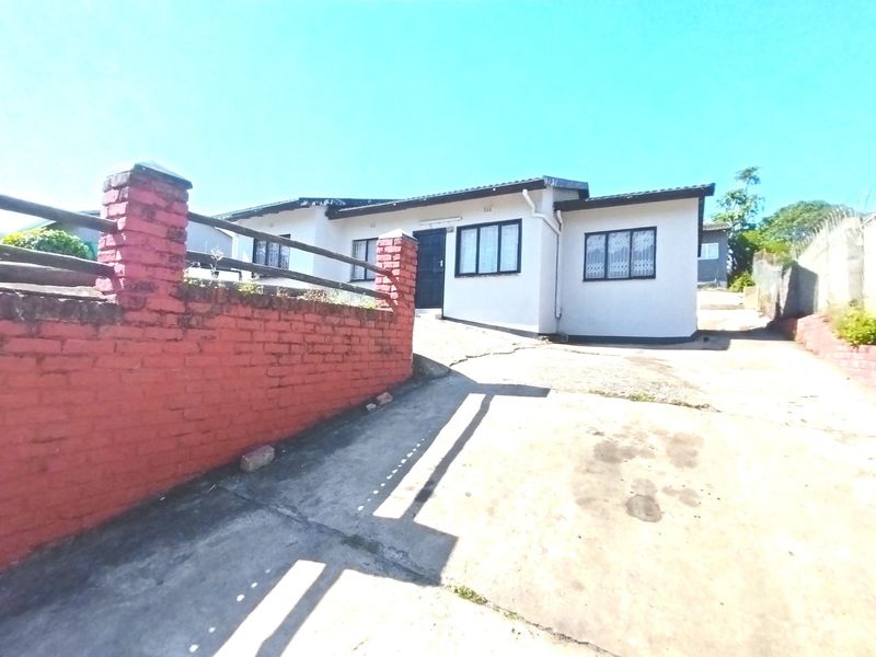 Front exterior view of a single-story house featuring a concrete driveway, brick boundary wall, and security-fitted windows.