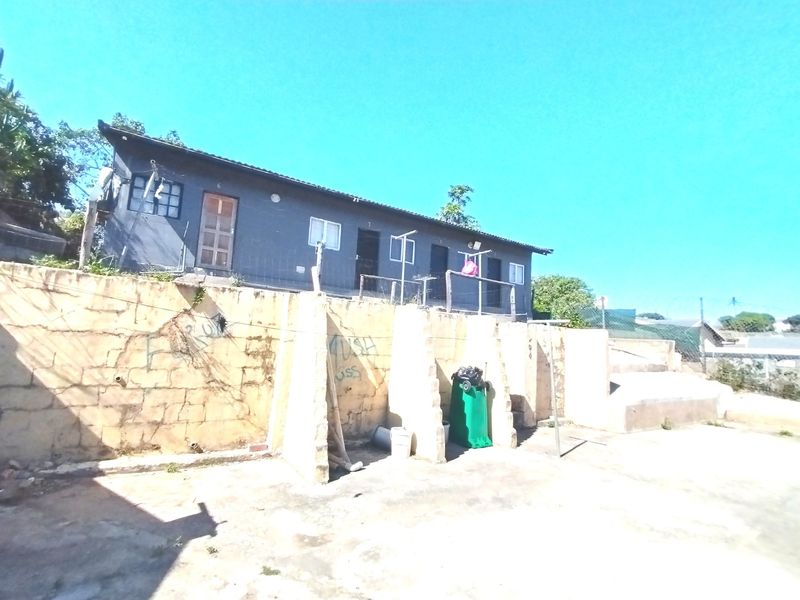 Rear exterior view of the property featuring a raised building structure above a weathered retaining wall with concrete paved area.