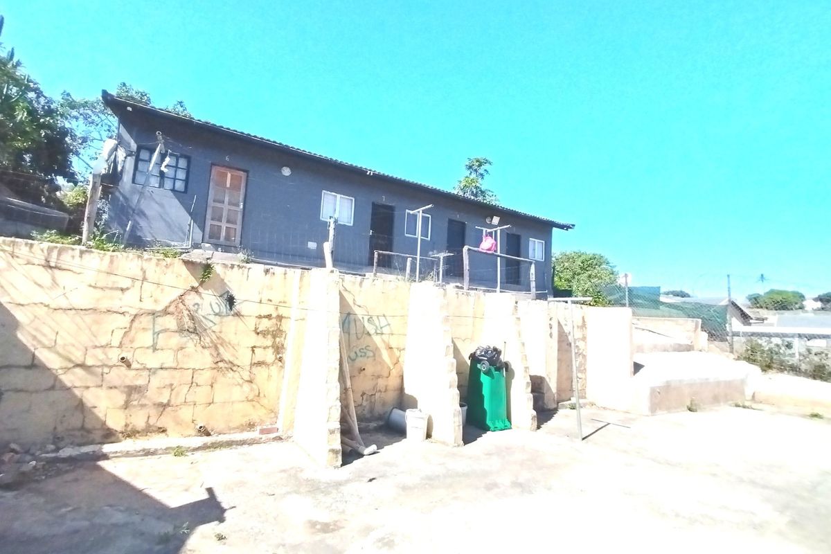 Rear exterior view of the property featuring a raised building structure above a weathered retaining wall with concrete paved area.