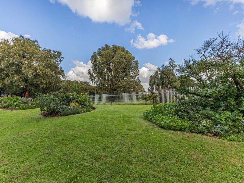 A well-maintained private garden featuring a lush green lawn, established garden beds, and secure metal perimeter fencing with integrated electric security wires.