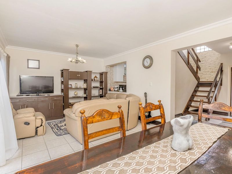 Open plan living and dining area featuring tiled floors, a staircase with wooden balustrades, and a view into the adjacent kitchen space.