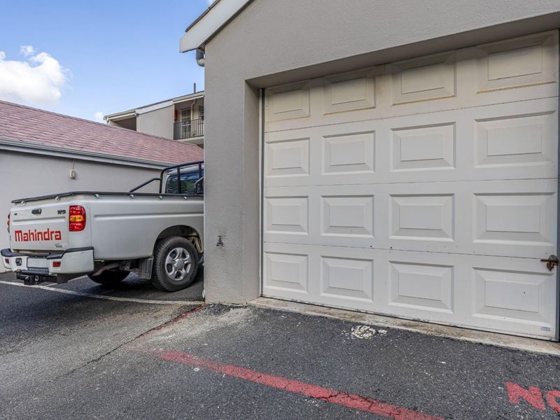 A view of a residential garage with a white sectional door and an exterior water tap, situated on an asphalt driveway.