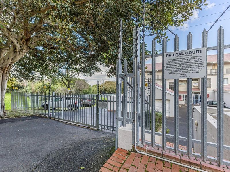 Front entrance view of the townhouse complex featuring a secure galvanized steel gate, electric fencing, and paved driveway access.