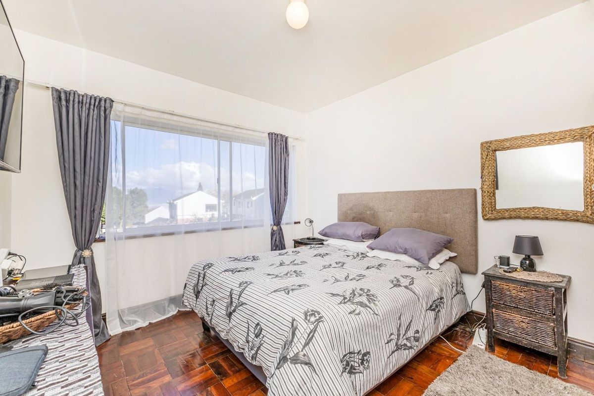 A well-lit bedroom featuring classic parquet flooring and a large window providing natural light and neighborhood views.