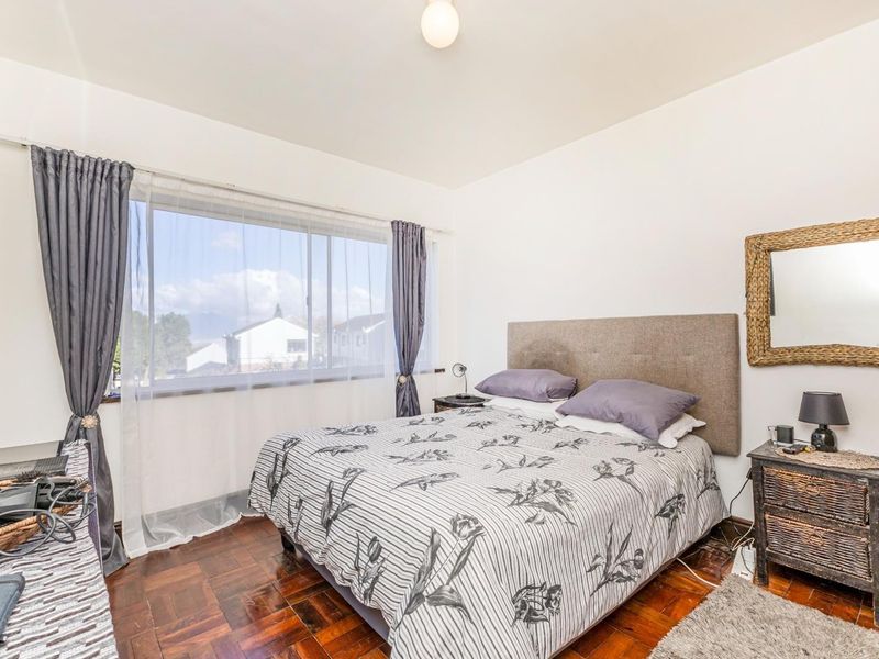A well-lit bedroom featuring classic parquet flooring and a large window providing natural light and neighborhood views.