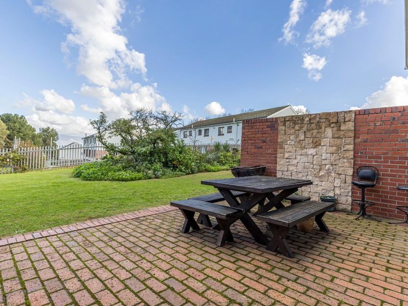 A private outdoor patio area featuring brick paving, a stone-clad feature wall, and a well-maintained lawn with secure perimeter fencing.