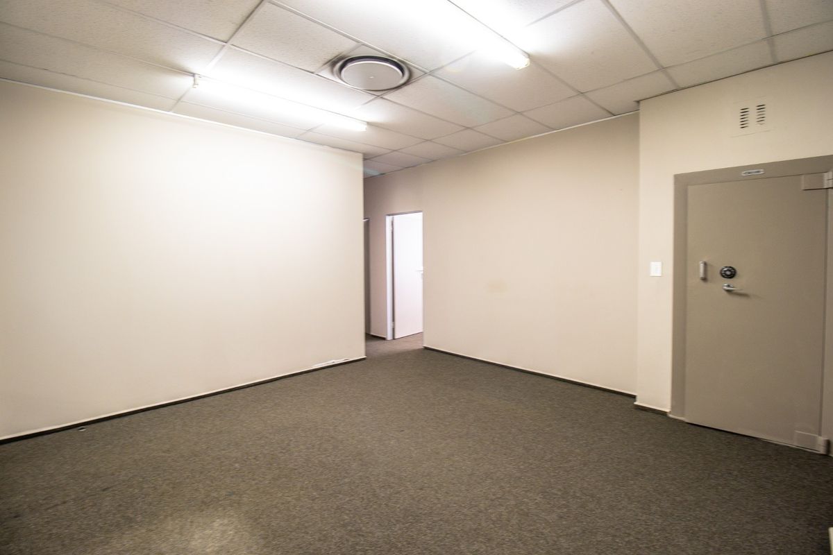 A vacant commercial office space featuring neutral walls, carpeted flooring, suspended ceiling lighting, and a secure heavy-duty steel vault door.