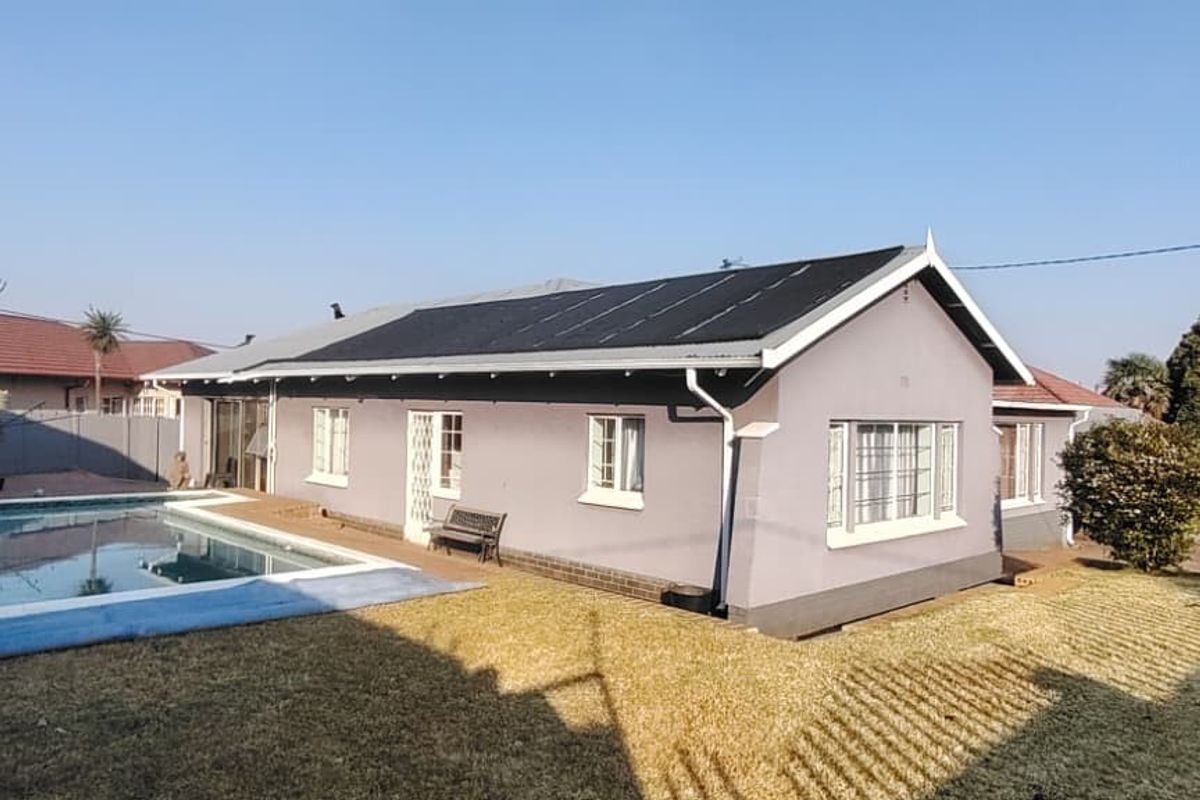 Rear exterior view of the house featuring a swimming pool, paved surround, and roof-mounted solar panels set within a private garden area.