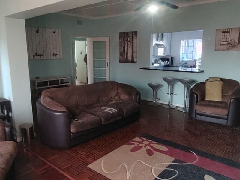 Open plan living area featuring classic parquet flooring, a breakfast bar pass-through to the kitchen, and ceiling fan, creating a connected and functional space.