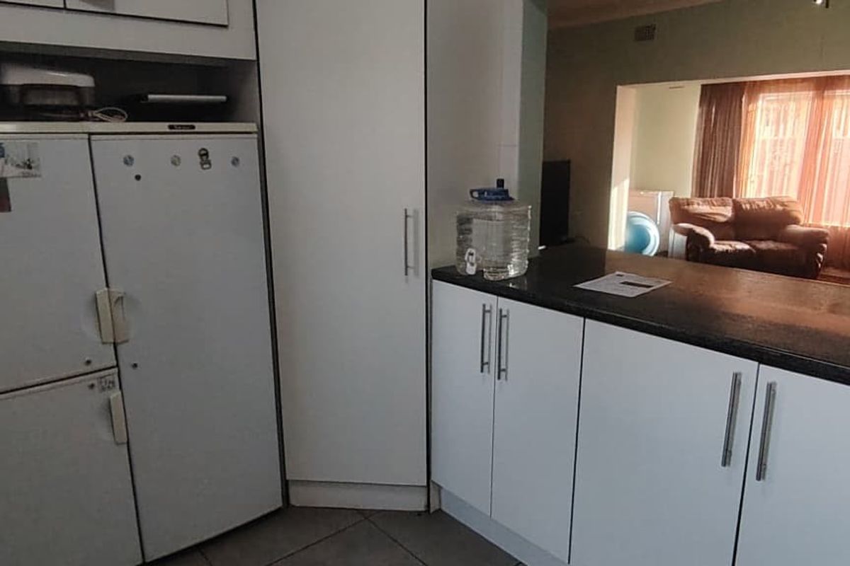 A functional kitchen area featuring white cabinetry, dark laminate countertops, and tiled flooring, with an open-plan layout connecting to the adjacent living space.