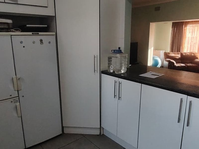 A functional kitchen area featuring white cabinetry, dark laminate countertops, and tiled flooring, with an open-plan layout connecting to the adjacent living space.