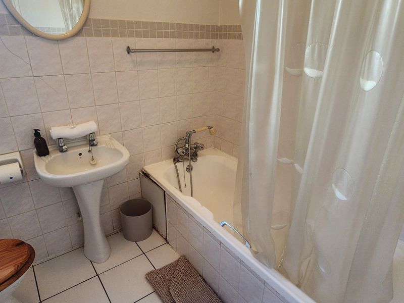 A functional bathroom featuring a pedestal basin, bathtub with shower mixer, and neutral wall and floor tiling.