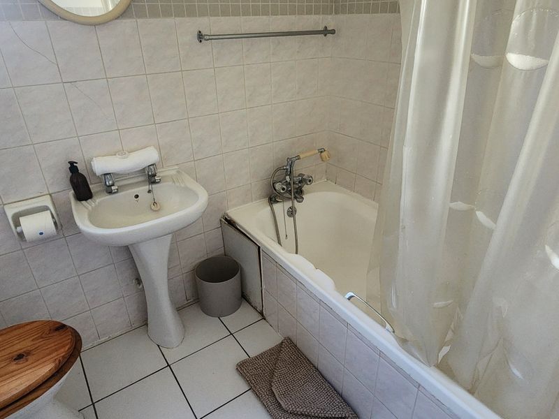 A dated bathroom featuring a pedestal basin, bathtub with shower mixer, and tiled finishes, requiring cosmetic updates to improve its overall condition.