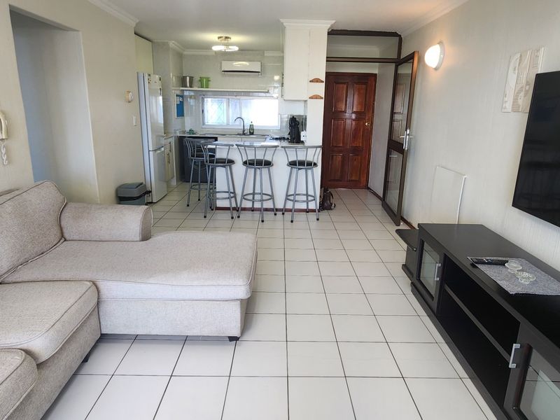 Open-plan living area featuring tiled flooring, a breakfast bar, and an integrated kitchen space with cabinetry and sink.