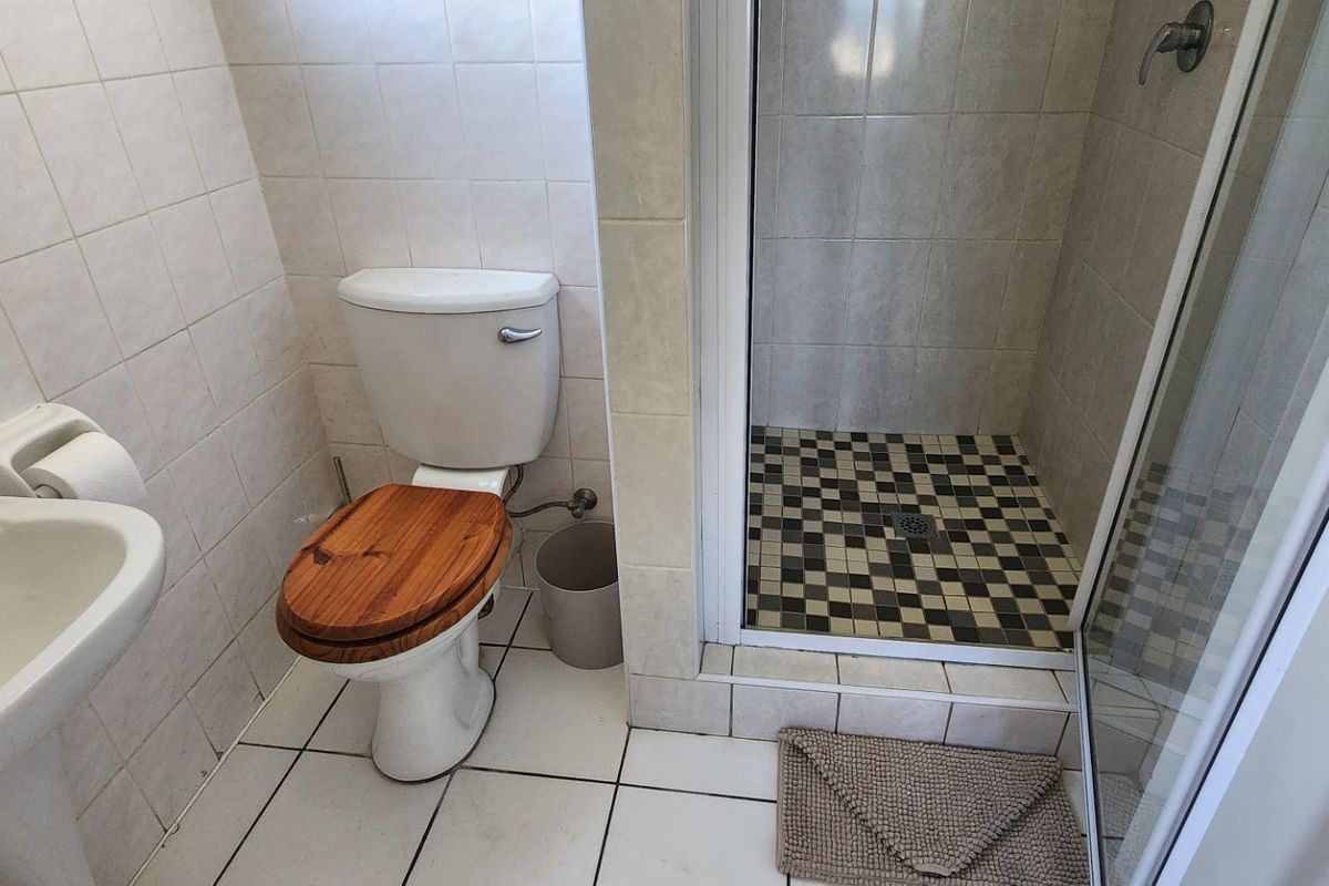 A functional bathroom featuring a pedestal basin, standard toilet, and a separate shower enclosure with tiled finishes.