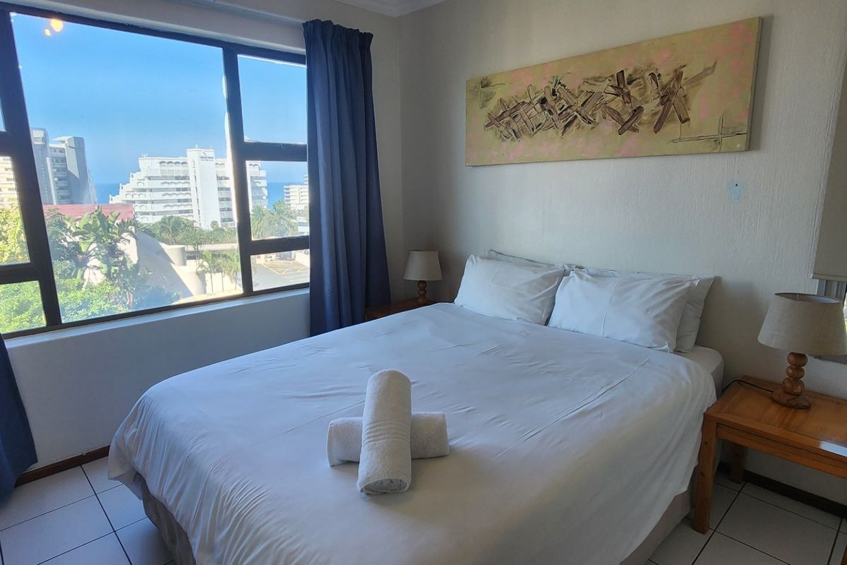 A bright bedroom featuring large windows with coastal views, tiled flooring, and neutral wall finishes.
