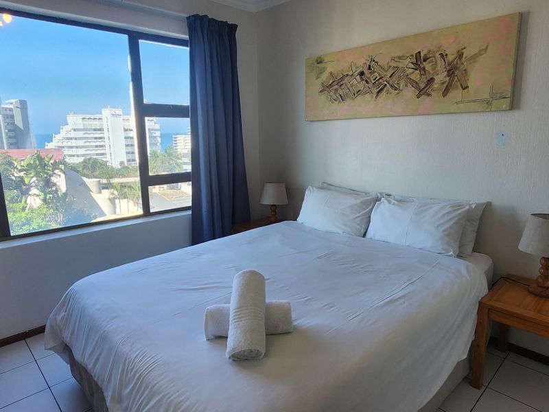 A bright bedroom featuring large windows with coastal views, tiled flooring, and neutral wall finishes.