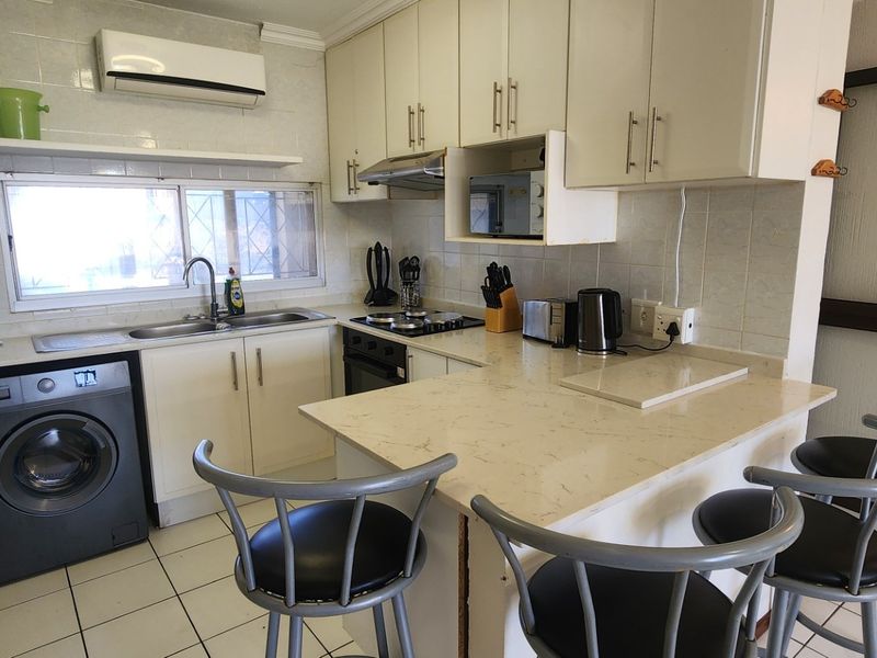 A functional kitchen featuring built-in cabinetry, stone countertops, a breakfast bar, and integrated appliances, with tiled flooring and backsplash throughout.