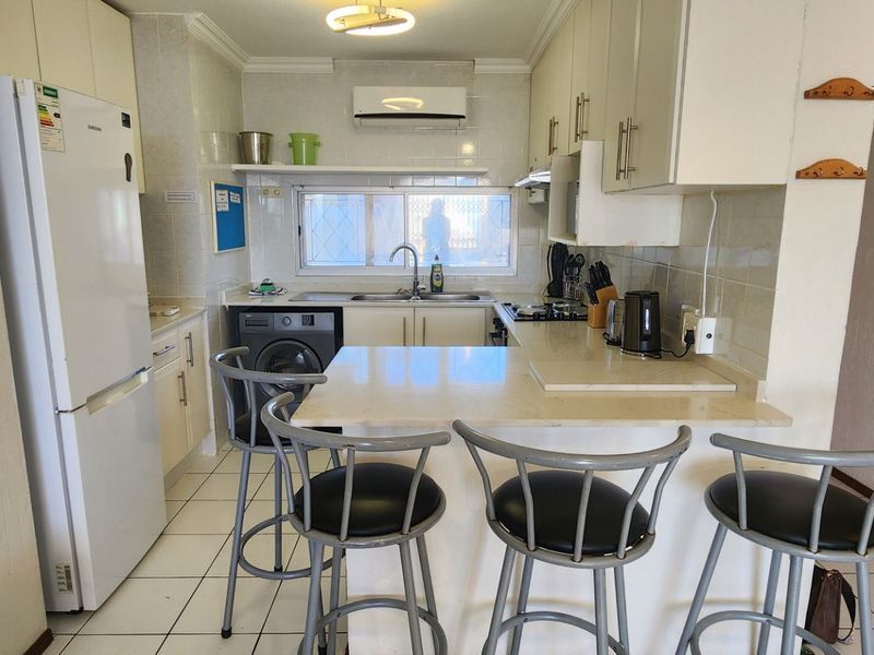 Functional kitchen featuring built-in cabinetry, stone countertops with a breakfast bar, tiled flooring, and a wall-mounted air conditioning unit.