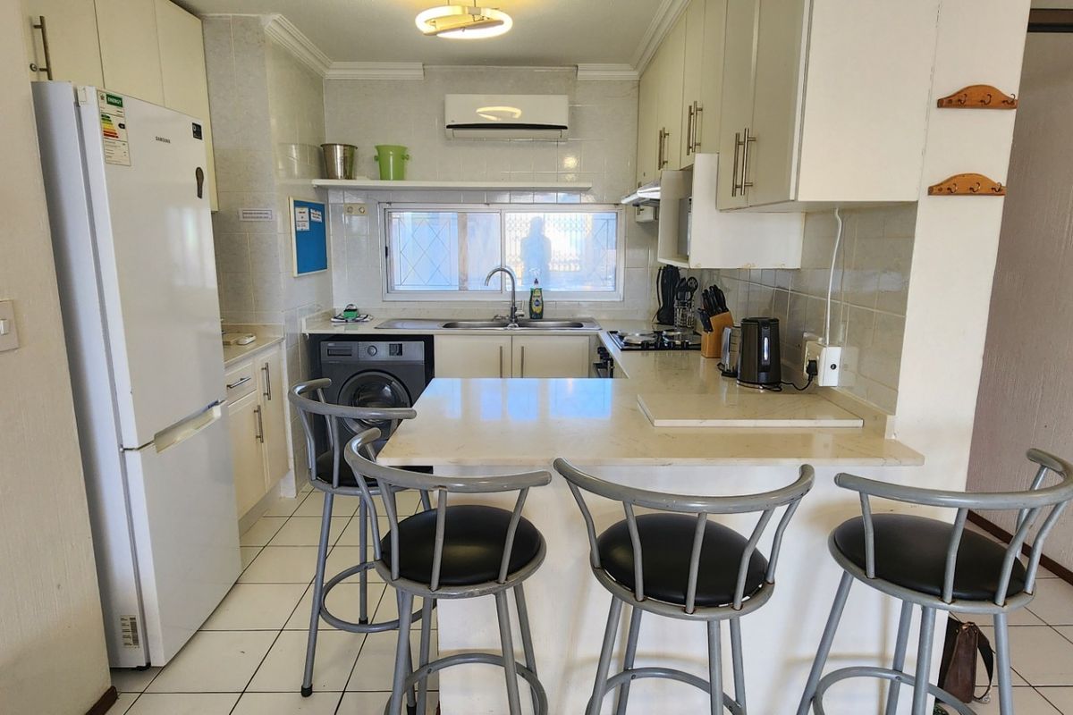 Functional kitchen featuring built-in cabinetry, stone countertops with a breakfast bar, tiled flooring, and a wall-mounted air conditioning unit.