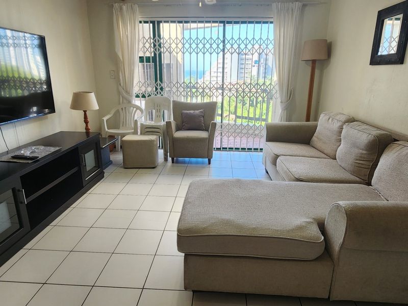 A living room featuring tiled flooring and a sliding glass door with a security gate, providing access to an outdoor area.