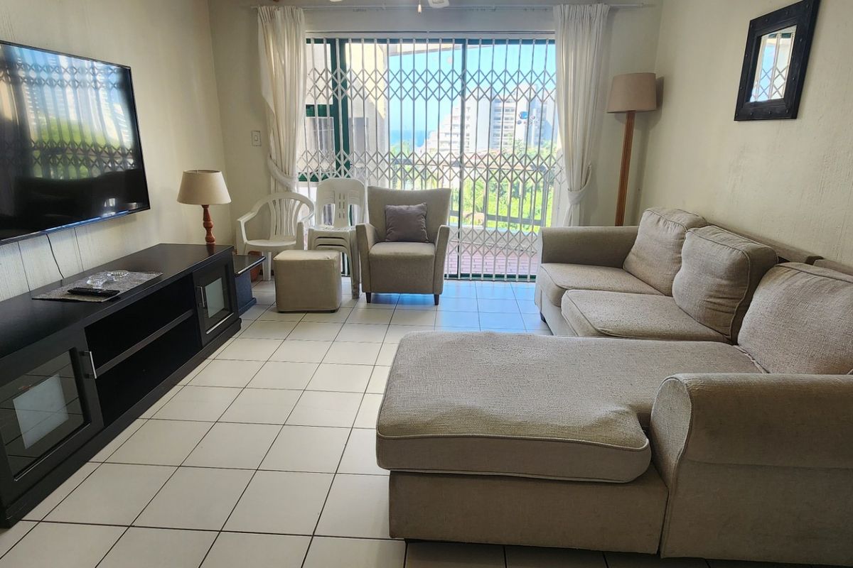 A living room featuring tiled flooring and a sliding glass door with a security gate, providing access to an outdoor area.