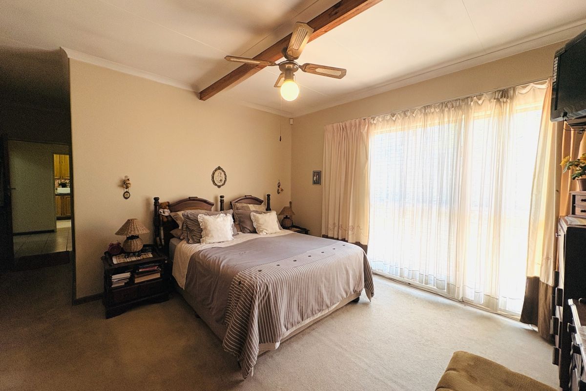 Spacious bedroom featuring a ceiling fan, exposed timber beam, and large sliding glass doors providing natural light.