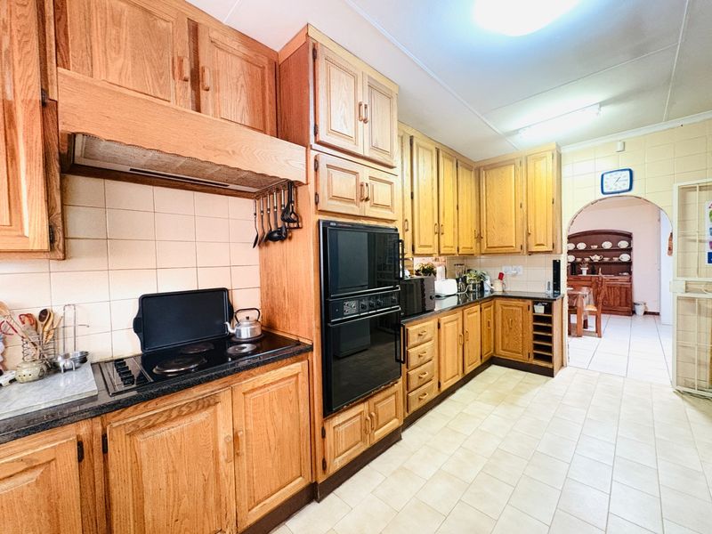 A traditional kitchen featuring extensive wooden cabinetry, built-in oven, electric hob, and tiled flooring, offering a functional layout with potential for modern updates.