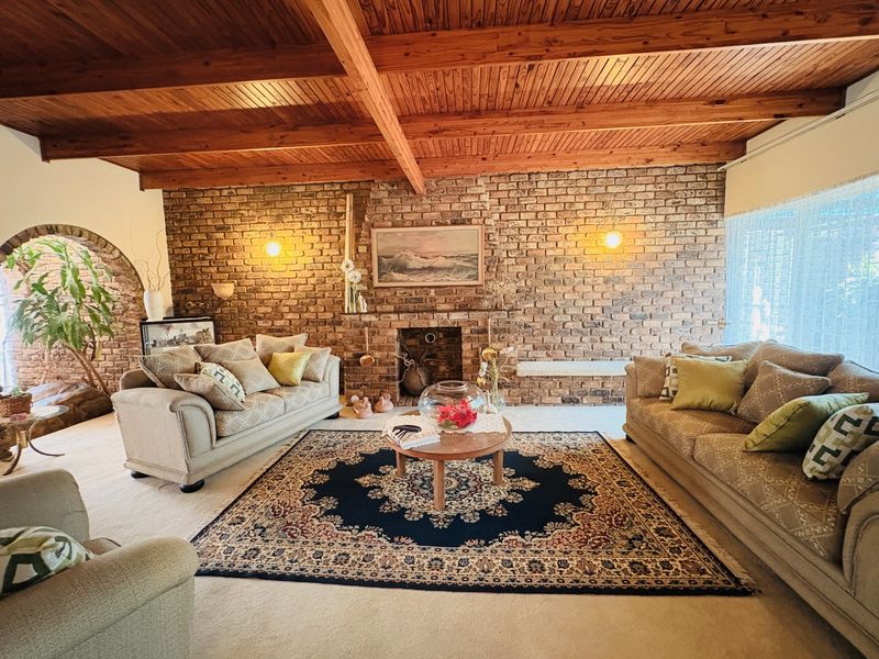 Spacious living room featuring a prominent brick fireplace, exposed timber beam ceiling, and a characterful brick feature wall with an arched entryway.