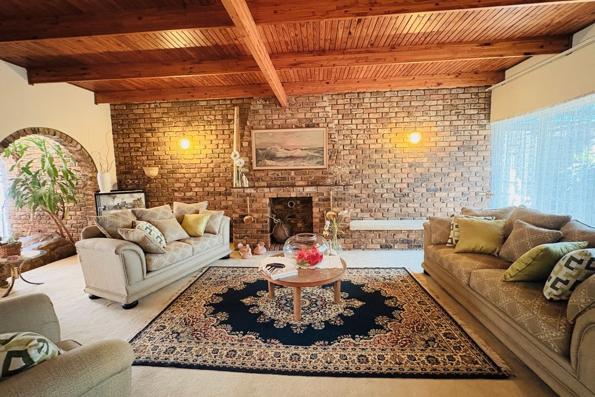 Spacious living room featuring a prominent brick fireplace, exposed timber beam ceiling, and a characterful brick feature wall with an arched entryway.