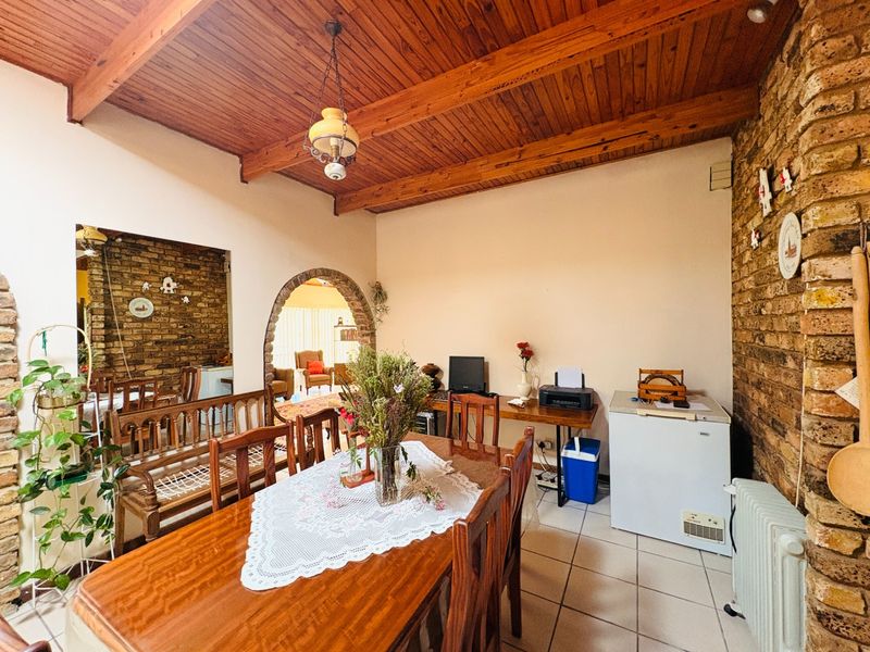 Dining room featuring exposed timber beam ceilings, rustic brick feature walls, and an arched doorway leading to an adjacent living space.