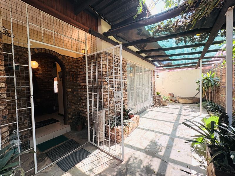 A covered outdoor patio area featuring stone paving, a pergola structure, and brick wall finishes, providing a sheltered entrance space.