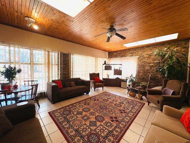 Spacious living room featuring a timber-clad ceiling, exposed brick wall, ceramic floor tiles, and a skylight, offering a warm and character-filled living space.