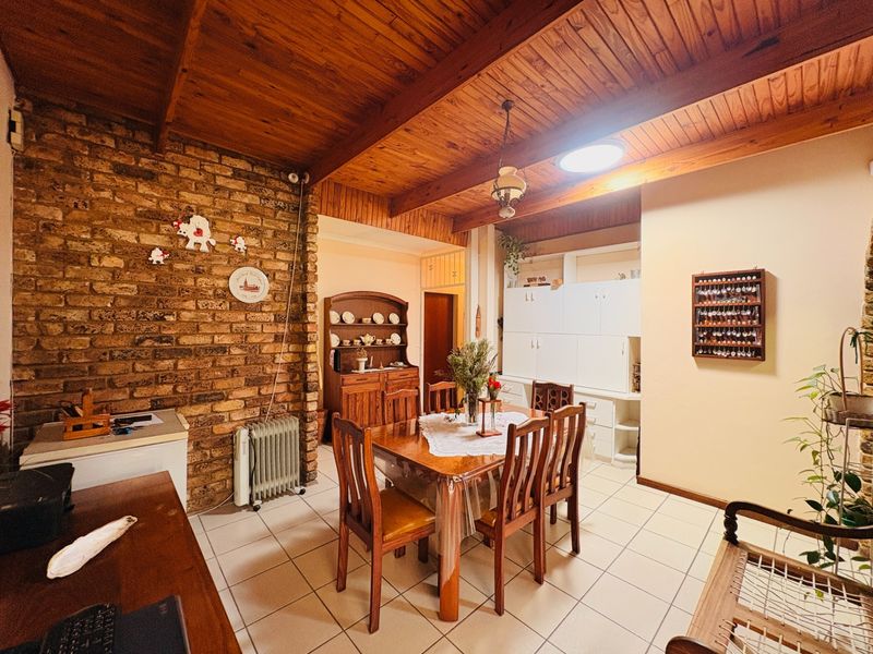 Dining area featuring exposed brick wall, timber beam ceiling, and tiled flooring with built-in storage cabinetry.