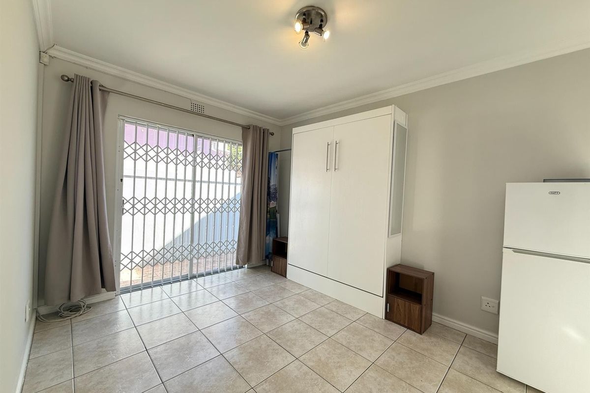 A clean, tiled bedroom featuring a built-in wall unit and a sliding glass door with a security gate leading to the exterior.
