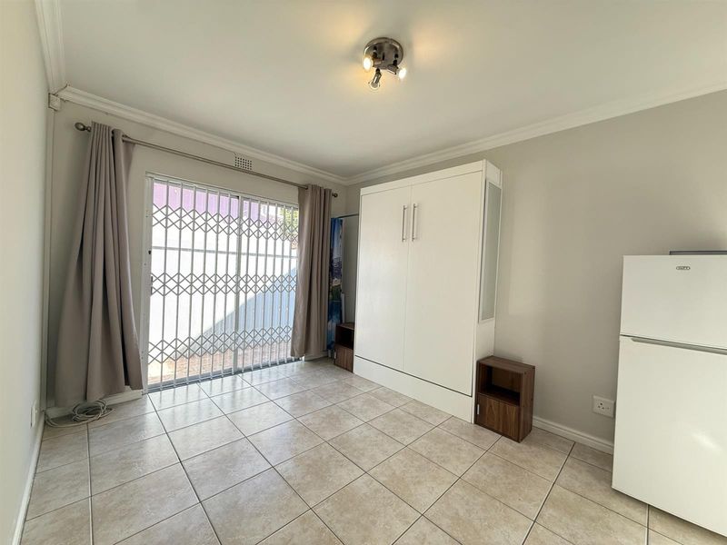 A clean, tiled bedroom featuring a built-in wall unit and a sliding glass door with a security gate leading to the exterior.