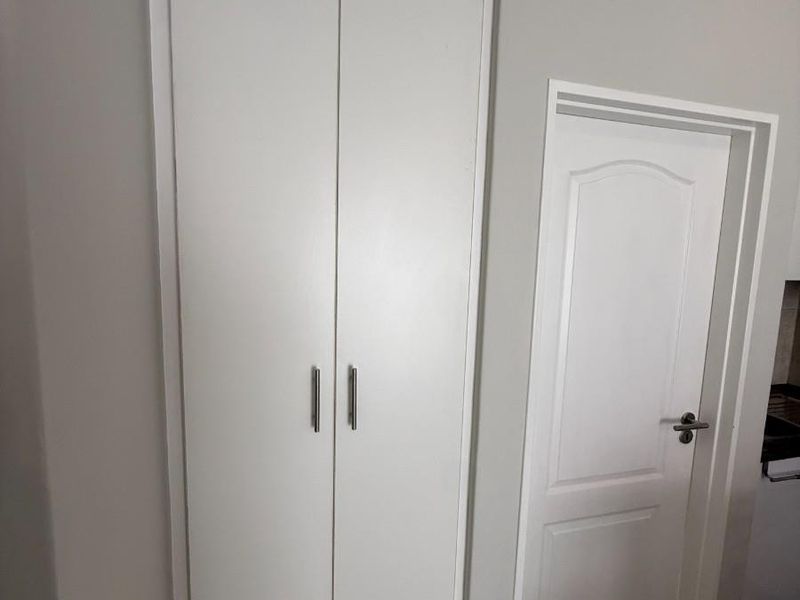 A clean hallway featuring a tall built-in cupboard, neutral wall finishes, decorative coving, and tiled flooring.