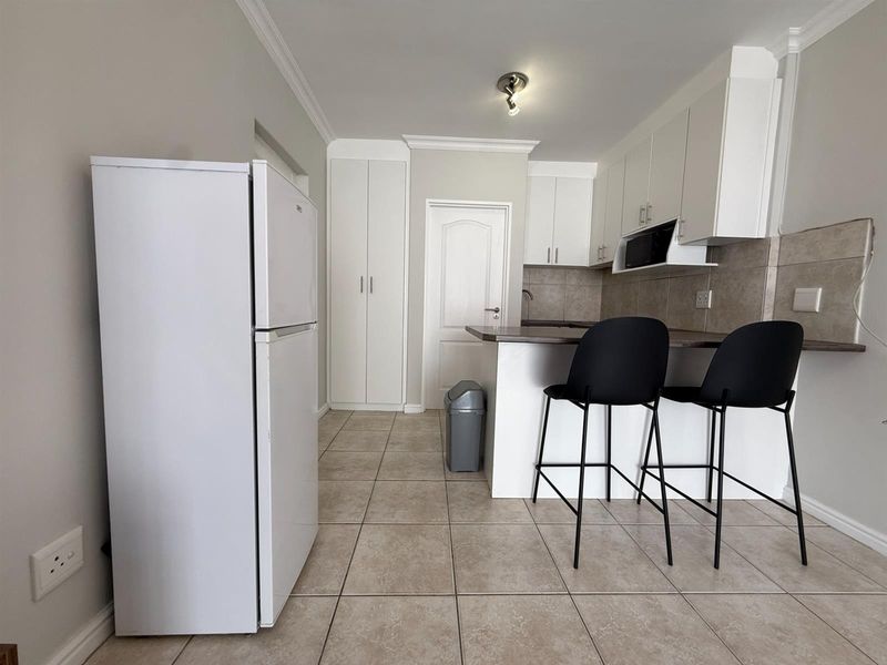 A functional kitchen featuring white cabinetry, a breakfast bar, tiled flooring, and a built-in pantry cupboard for additional storage.