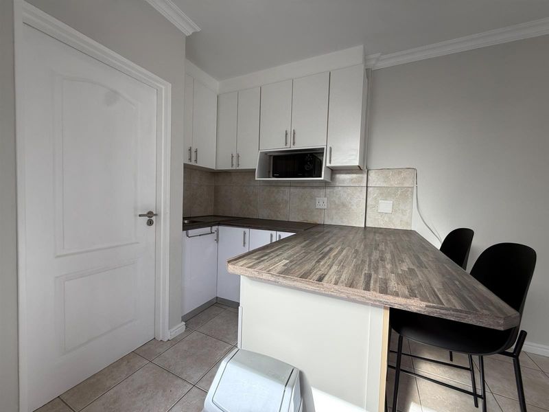 Compact kitchen featuring white cabinetry, wood-look laminate countertops, a breakfast bar, tiled backsplash, and tiled flooring.