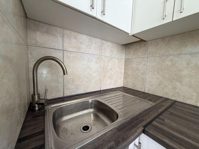 A compact kitchen prep area featuring a stainless steel sink, modern gooseneck faucet, dark laminate countertops, and neutral tiled backsplash.