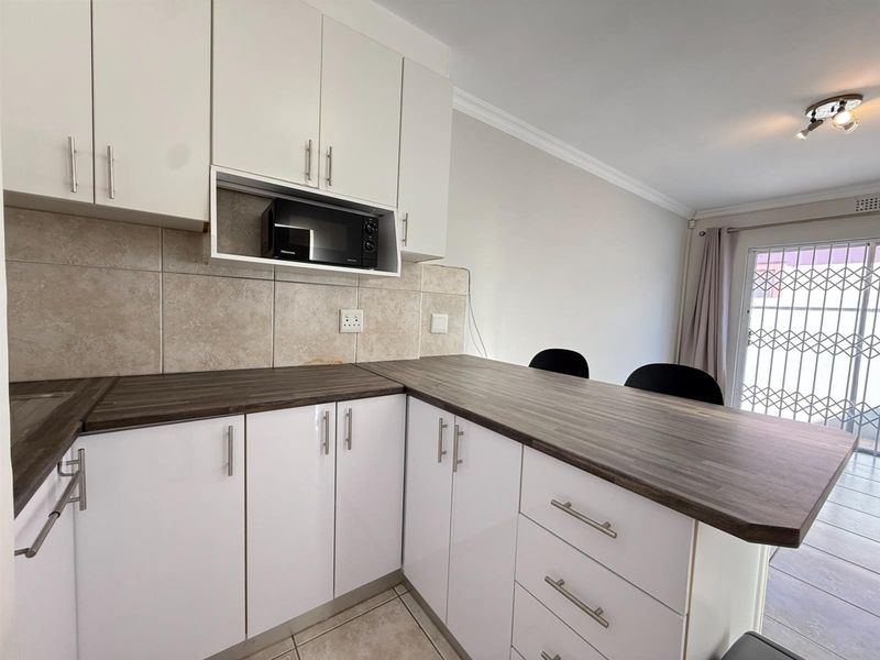Modern kitchen featuring white cabinetry, dark laminate countertops, a tiled backsplash, and a convenient breakfast bar area with access to the exterior.