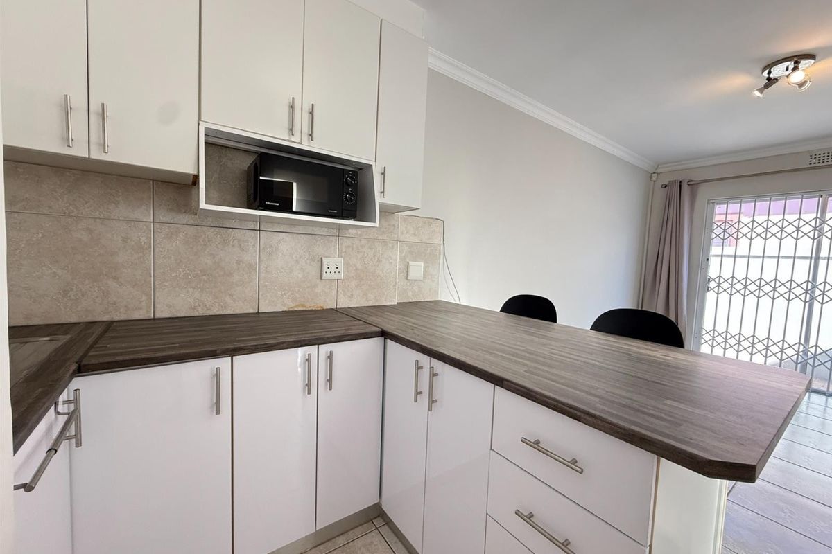 Modern kitchen featuring white cabinetry, dark laminate countertops, a tiled backsplash, and a convenient breakfast bar area with access to the exterior.