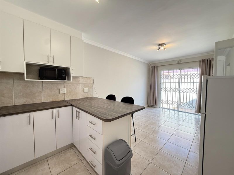 Open-plan kitchen and living area featuring white cabinetry, laminate countertops, tiled flooring, and a sliding door leading to the exterior.