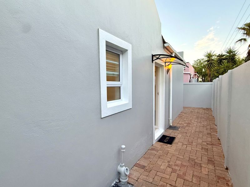 A clean side passage featuring paved flooring, a boundary wall, and a small protective awning over the entrance door.