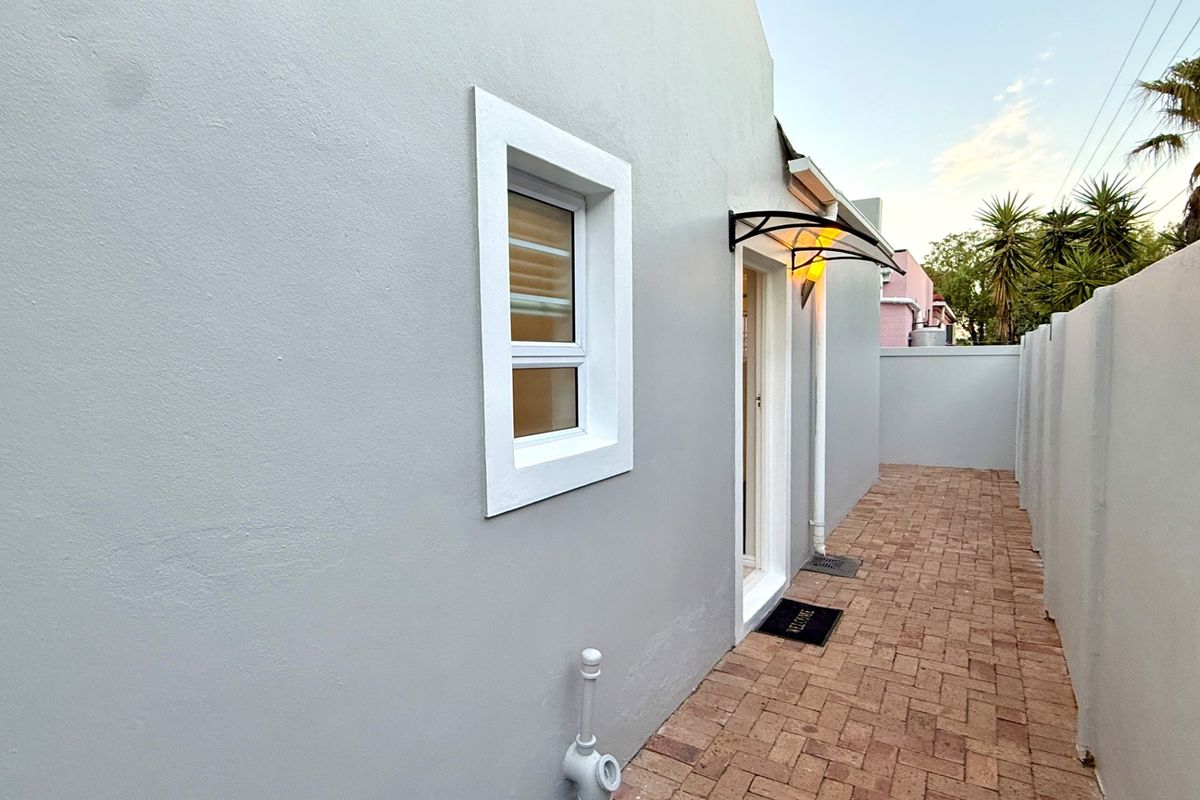 A clean side passage featuring paved flooring, a boundary wall, and a small protective awning over the entrance door.