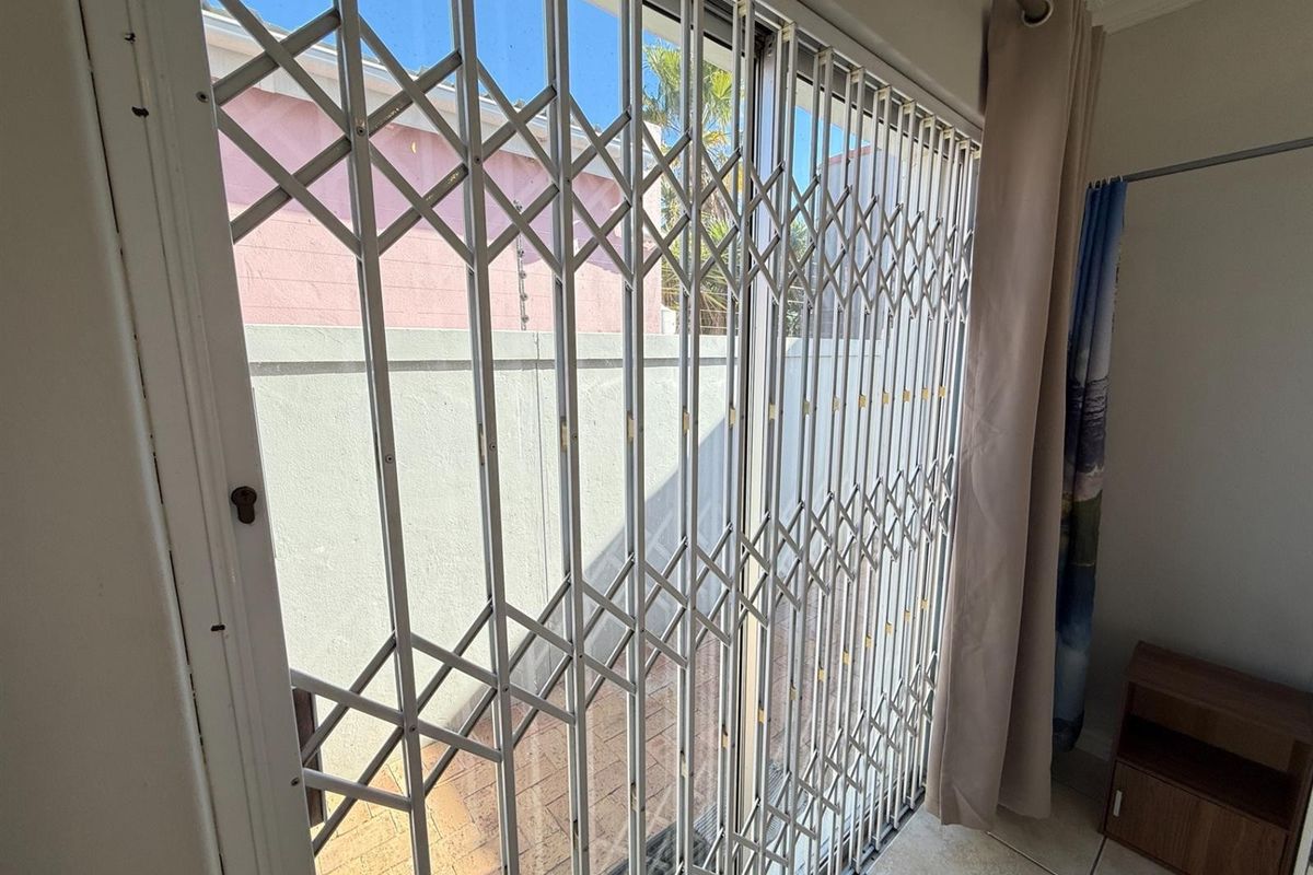 Interior view of a living area featuring a sliding glass door secured with a metal security gate, leading to an outdoor paved space.