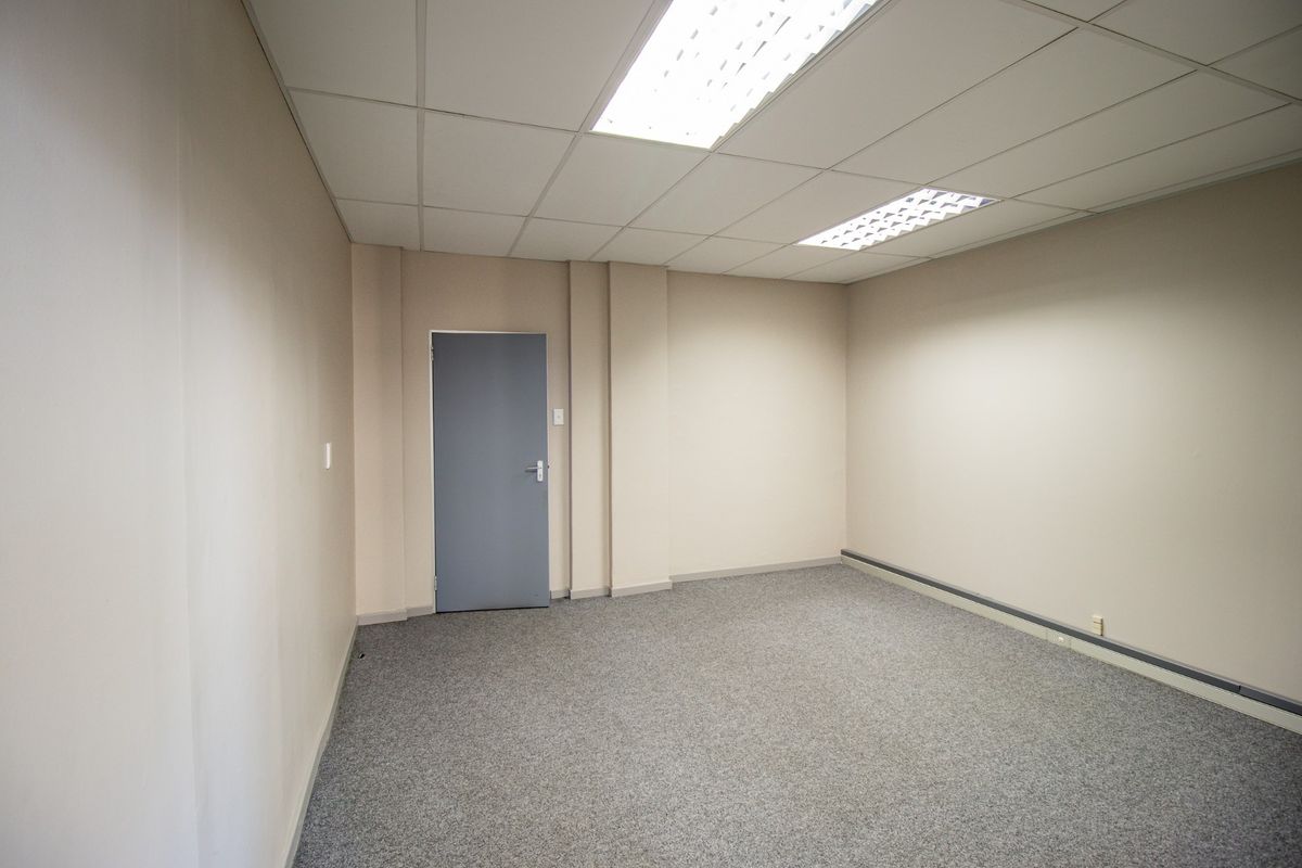 A clean, empty commercial office space featuring neutral walls, grey carpeting, and a suspended ceiling with recessed lighting.